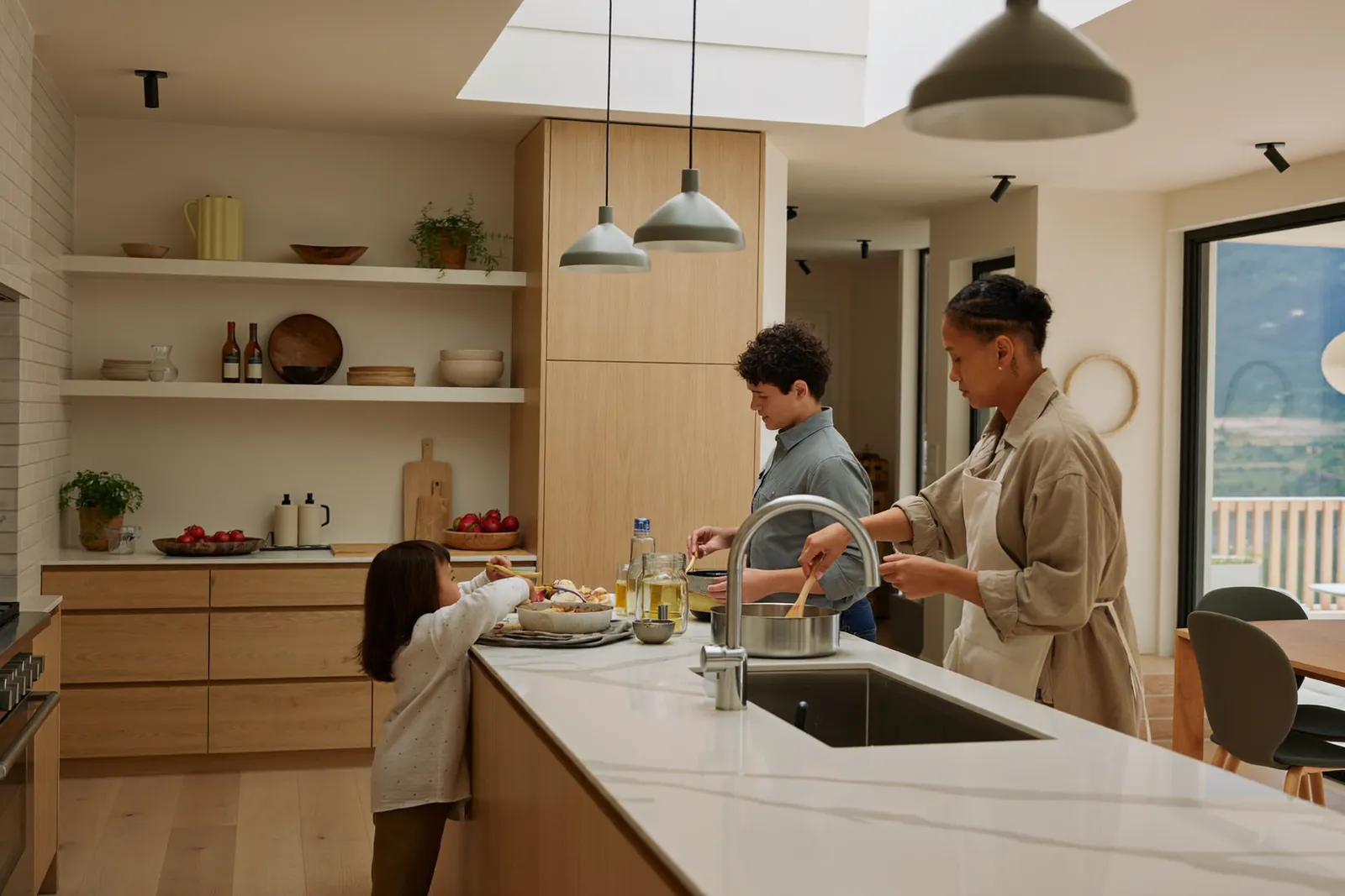 Familie kocht gemeinsam in einer hellen, offenen Küche, ein Kind hilft beim Rühren