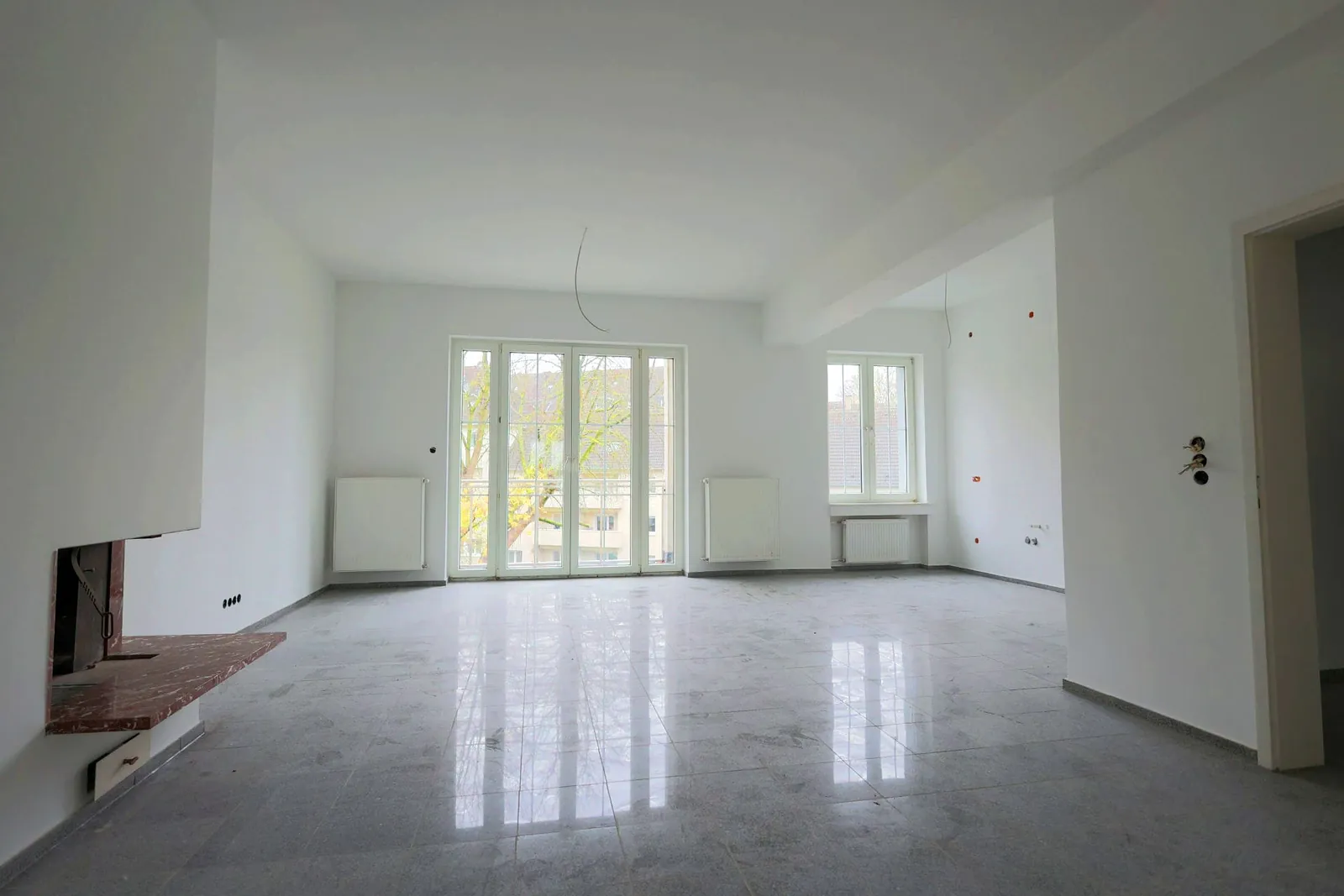 Heller Wohnraum im Bismarckhaus mit hohen Decken, großen Sprossenfenstern, Kamin und polierten Fliesen in Steinoptik