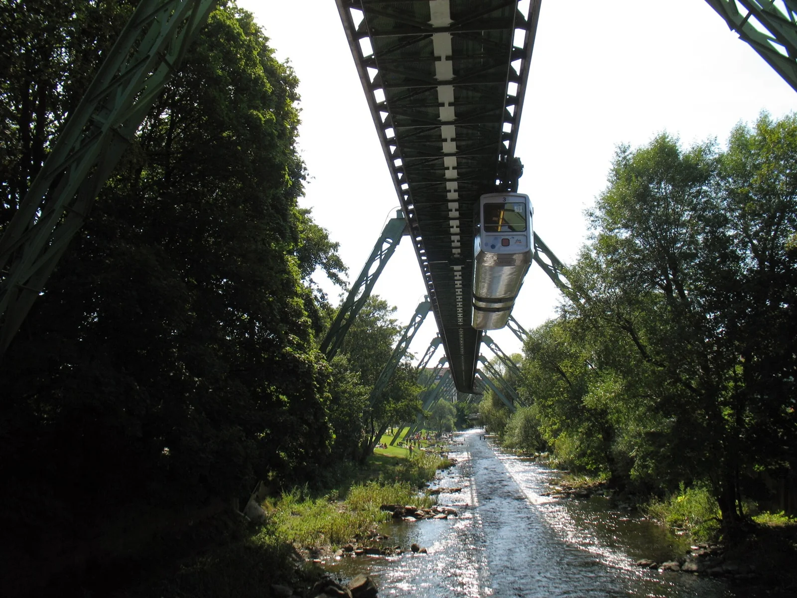 Die Wuppertaler Schwebebahn fährt in Oberbarmen über die grün gesäumte Wupper